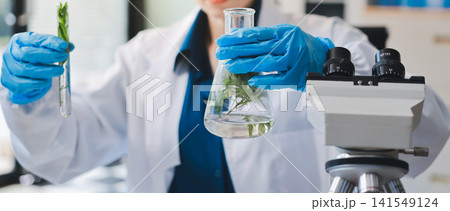 Scientists in lab coats work with plants in a modern lab, focusing on research and experimentation under bright, sterile conditions. Scientists in lab coats work with plants in a modern lab, focusing on research and experimentation under bright, sterile conditions. 141549124