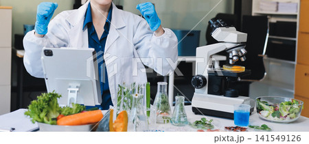 Scientists in lab coats work with plants in a modern lab, focusing on research and experimentation under bright, sterile conditions. 141549126