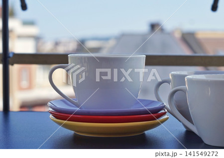 A white ceramic cup sits on stacked colorful saucers while another cup appears at the edge of the frame. The scene symbolizes companionship, shared conversation, and warmth in everyday home life A white ceramic cup sits on stacked colorful saucers while another cup appears at the edge of the frame. The scene symbolizes companionship, shared conversation, and warmth in everyday home life 141549272