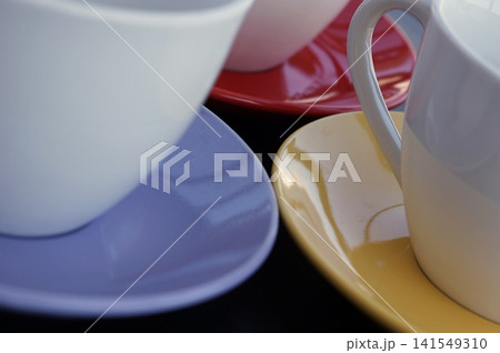 A close-up view highlights white ceramic cups standing on yellow and purple saucers. The composition reflects warmth, hospitality, and the pleasure of quiet conversations. A close-up view highlights white ceramic cups standing on yellow and purple saucers. The composition reflects warmth, hospitality, and the pleasure of quiet conversations. 141549310