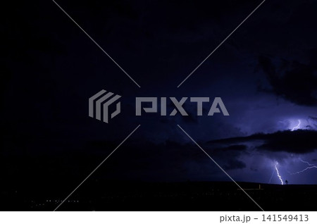 A narrow lightning bolt appears below layered storm clouds in a nearly black night sky. Minimal nocturnal scene symbolizes uncertainty, tension, and sudden natural energy. A narrow lightning bolt appears below layered storm clouds in a nearly black night sky. Minimal nocturnal scene symbolizes uncertainty, tension, and sudden natural energy. 141549413