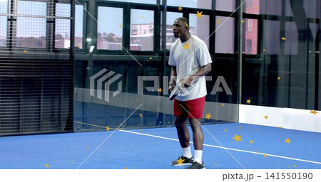 Holding padel racket, man wearing gray T-shirt and red shorts on blue court, copy space 141550190