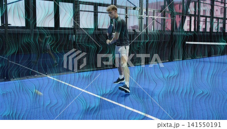 Swinging man dark shirt white shorts hitting yellow ball with racket on blue court, mesh fencing 141550191