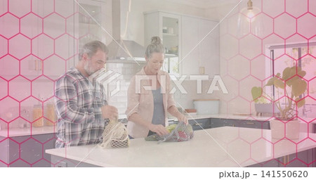 Unpacking couple placing mesh bags on quartz island in kitchen with pink hex, in casual shirts 141550620