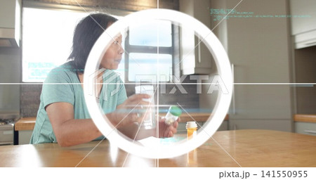 Senior woman in green tee holding green-lid pill bottle, water glass in kitchen, ring crosshair Senior woman in green tee holding green-lid pill bottle, water glass in kitchen, ring crosshair 141550955