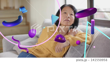 Reclining senior Chinese wearing mustard sweater and blue jeans on sofa, purple 3D shapes floating 141550958