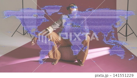 Sitting Indian model wearing shades, posing on pouf in studio with purple world map overlay casting 141551229