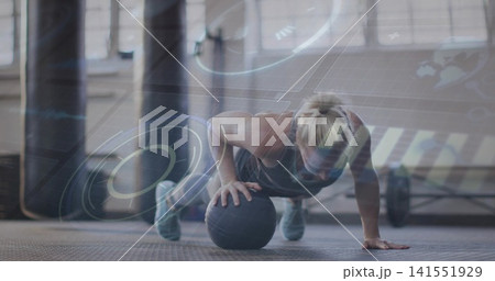 Performing mid-adult woman doing medicine-ball push-up at gym, wearing dark athletic gear, HUD Performing mid-adult woman doing medicine-ball push-up at gym, wearing dark athletic gear, HUD 141551929