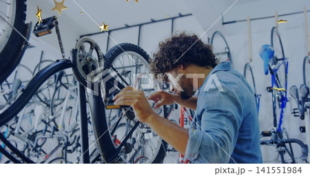 Repairing mechanic adjusting rear wheel and cassette on black bike in shop wall racks, denim-shirt Repairing mechanic adjusting rear wheel and cassette on black bike in shop wall racks, denim-shirt 141551984
