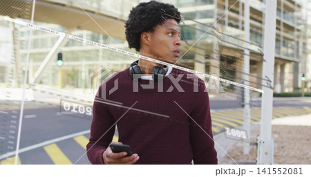 Standing man looking right on city sidewalk with smartphone, wearing maroon sweater and headphones Standing man looking right on city sidewalk with smartphone, wearing maroon sweater and headphones 141552081