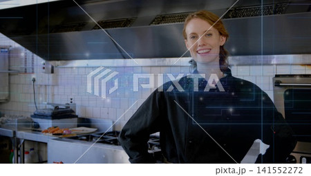 Posing female chef in black coat, standing in kitchen with stove, plate, blue HUD, copy space Posing female chef in black coat, standing in kitchen with stove, plate, blue HUD, copy space 141552272