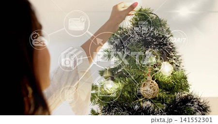 Placing woman in cream sweater adjusting rattan ornament on Christmas tree at home, with UI overlay 141552301
