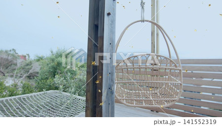 Swaying woven rattan egg chair hanging from overhead beam on beachfront deck, with net hammock Swaying woven rattan egg chair hanging from overhead beam on beachfront deck, with net hammock 141552319