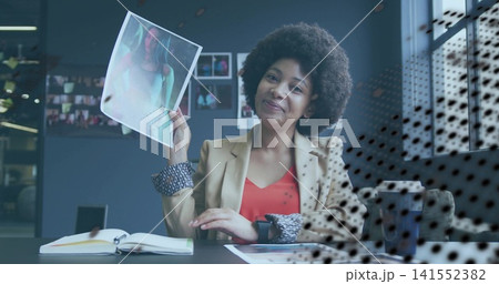 Displaying woman wearing tan blazer angling glossy print at studio desk, with smartwatch Displaying woman wearing tan blazer angling glossy print at studio desk, with smartwatch 141552382