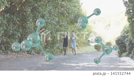 Walking two women in black-grey sleeveless outfits holding bottle along garden path with molecules Walking two women in black-grey sleeveless outfits holding bottle along garden path with molecules 141552744