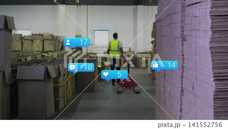 Pushing worker in hi-vis vest using red pallet jack down aisle, with tall cardboard stack, overlays Pushing worker in hi-vis vest using red pallet jack down aisle, with tall cardboard stack, overlays 141552756