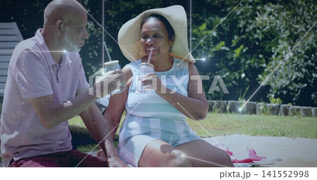 Clinking senior woman wearing wide sun hat and striped dress on backyard patio, holding jar cups Clinking senior woman wearing wide sun hat and striped dress on backyard patio, holding jar cups 141552998