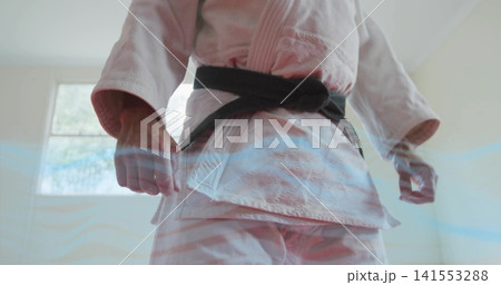 Standing martial artist in white gi and black belt clenching fists at dojo, rectangular window Standing martial artist in white gi and black belt clenching fists at dojo, rectangular window 141553288