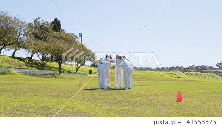 Huddling seven female players in white uniforms linking arms on grassy field, with orange cones Huddling seven female players in white uniforms linking arms on grassy field, with orange cones 141553325