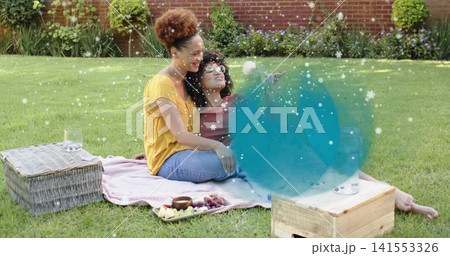 Sitting two mid-adult women sharing fruit on woven blanket on backyard lawn, wicker basket Sitting two mid-adult women sharing fruit on woven blanket on backyard lawn, wicker basket 141553326