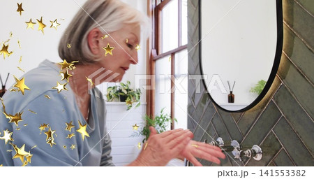Washing hands senior woman in pale-blue top at bathroom sink, showing mirror and faucet, gold-stars Washing hands senior woman in pale-blue top at bathroom sink, showing mirror and faucet, gold-stars 141553382