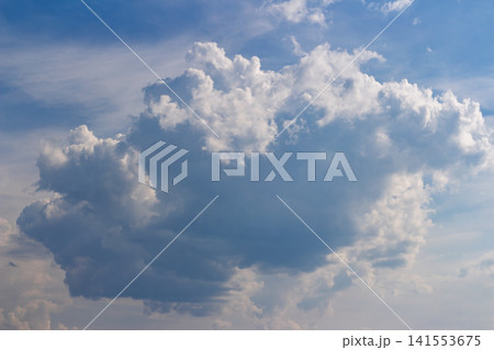 Huge fluffy white cumulus cloud floating in the clear blue sky, majestic airy formation illuminated by bright sunlight, a peaceful and scenic meteorological atmosphere overhead Huge fluffy white cumulus cloud floating in the clear blue sky, majestic airy formation illuminated by bright sunlight, a peaceful and scenic meteorological atmosphere overhead 141553675