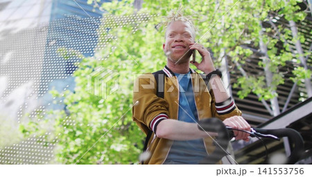 Talking man wearing mustard bomber jacket and blue shirt holding smartphone and bicycle at plaza Talking man wearing mustard bomber jacket and blue shirt holding smartphone and bicycle at plaza 141553756