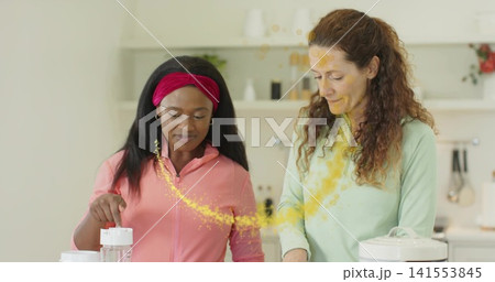 Mixing two women in pink zip-front and light-green top at home kitchen, with clear blender jar 141553845