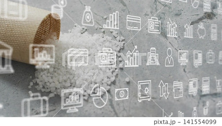 Spilling kraft paper cone scattering coarse white salt on gray stone surface, finance icons overlay 141554099