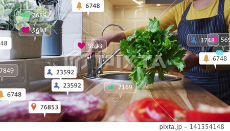 Holding cook in striped apron yellow top, showing greens over sink with social overlays, copy space 141554148