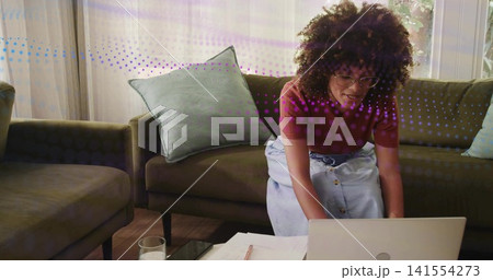 Leaning mid-adult woman wearing maroon top, denim skirt, typing on laptop at home sofa, with papers Leaning mid-adult woman wearing maroon top, denim skirt, typing on laptop at home sofa, with papers 141554273