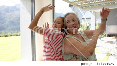 Laughing mom and daughter pressing glass door at home, wearing striped shirt, floral top, watch 141554525