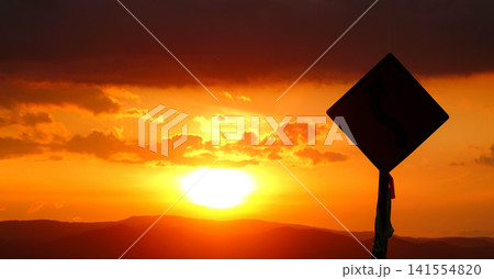 穏やかな秋の夕暮れと緩やかに沈む太陽とシルエットになった標識 141554820