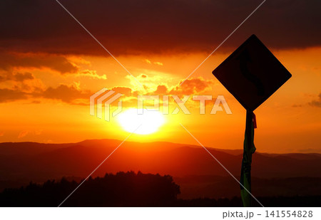 穏やかな秋の夕暮れと緩やかに沈む太陽とシルエットになった標識 141554828