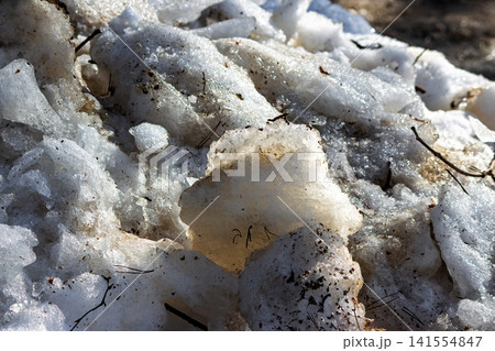 Chunky, grimy snow piles gradually thawing at the roadside, glimmering with ice crystals in early spring, a messy seasonal transition 141554847