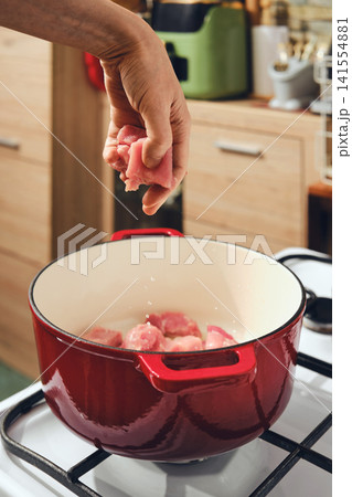 Cook adds meat to pot on stove in a kitchen setting during meal preparation session 141554881