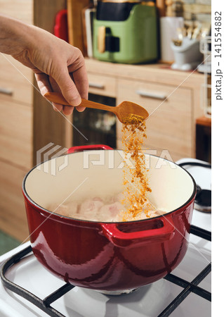 Cooking in a kitchen with spices being added to a pot on the stove in the afternoon 141554882
