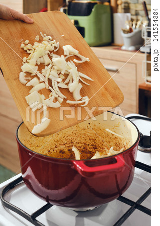 Chopping onions and adding them to a pot on the stove in a home kitchen setting 141554884