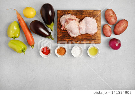 Cooking ingredients on gray surface with vegetables, chicken thighs and spices set for preparation Cooking ingredients on gray surface with vegetables, chicken thighs and spices set for preparation 141554905