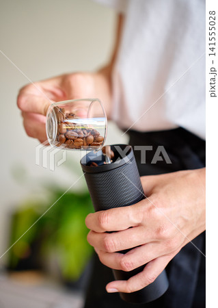 Person pouring coffee beans into manual grinder for home brewing Person pouring coffee beans into manual grinder for home brewing 141555028