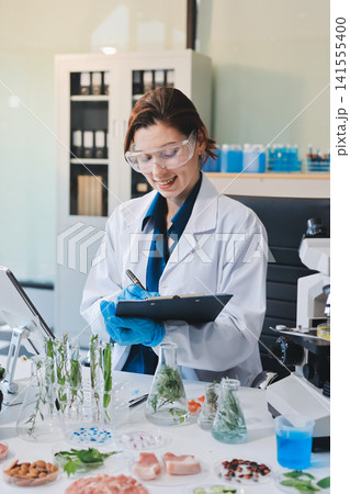 Scientists in lab coats work with plants in a modern lab, focusing on research and experimentation under bright, sterile conditions. 141555400