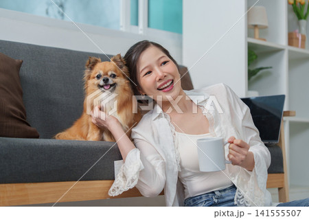 Asian woman relaxing with dog on living room couch with coffee mug for pet companionship concept Asian woman relaxing with dog on living room couch with coffee mug for pet companionship concept 141555507
