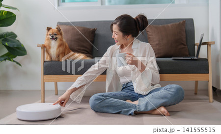 Asian woman pressing button on robot vacuum cleaner at home living room Asian woman pressing button on robot vacuum cleaner at home living room 141555515