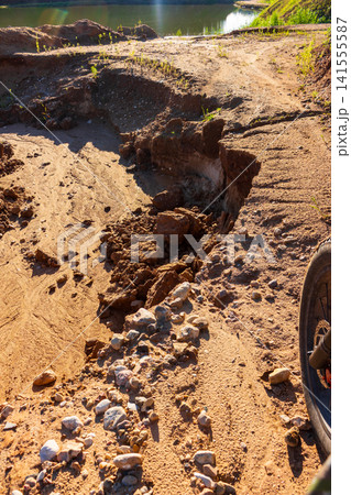 Close-up of a bicycle wheel facing a sandy track erosion, sharp earth edge blocking the path on a sunny day at a lake shore, adventurous cycling obstacle on a rough dirt trail Close-up of a bicycle wheel facing a sandy track erosion, sharp earth edge blocking the path on a sunny day at a lake shore, adventurous cycling obstacle on a rough dirt trail 141555587