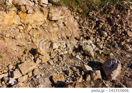 Rough limestone quarry wall with scattered rocks, loose gravel, and rugged terrain, showcasing raw geological texture and the natural earthy tones of an abandoned mining site Rough limestone quarry wall with scattered rocks, loose gravel, and rugged terrain, showcasing raw geological texture and the natural earthy tones of an abandoned mining site 141555606
