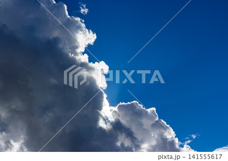 Dramatic sun rays breaking through heavy fluffy storm clouds, creating a vibrant contrast against the deep blue sky, perfect for nature concepts and meteorological backgrounds Dramatic sun rays breaking through heavy fluffy storm clouds, creating a vibrant contrast against the deep blue sky, perfect for nature concepts and meteorological backgrounds 141555617