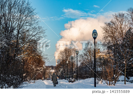 Vibrant winter scene with thick steam plume rising above snow-covered trees under a bright blue sky, single pedestrian walks down a frosty path Vibrant winter scene with thick steam plume rising above snow-covered trees under a bright blue sky, single pedestrian walks down a frosty path 141555889