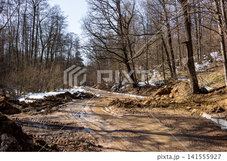 Muddy, rutted country road under construction in early spring. Bare trees line the path, with remnants of snow and a challenging detour ahead Muddy, rutted country road under construction in early spring. Bare trees line the path, with remnants of snow and a challenging detour ahead 141555927