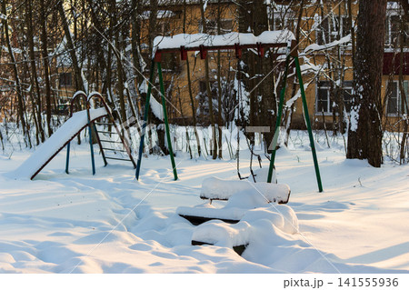 An old playground, including a slide and swings covered in thick white snow, sits quietly in a winter park setting at sunset An old playground, including a slide and swings covered in thick white snow, sits quietly in a winter park setting at sunset 141555936