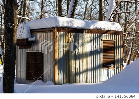 Frosty winter scene featuring a corrugated metal utility cabin, its roof laden with fresh snow and walls decorated with long, sharp icicles. Stark light 141556064